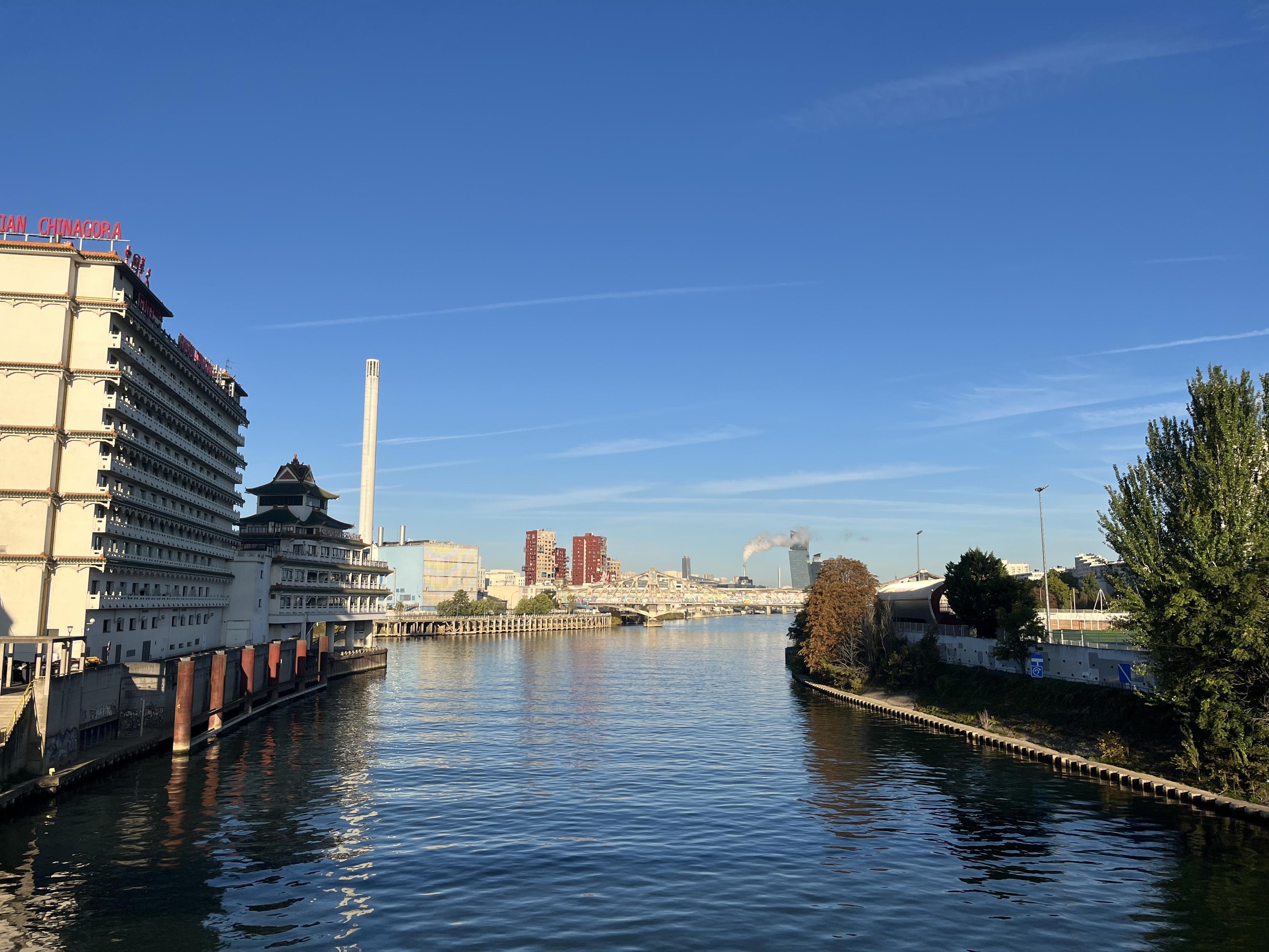Vue du confluent de la Marne et de la Seine depuis une passerelle à Alfortville. Un hôtel foutraque à gauche d’inspiration chinoise, le Huatian Chinagora, une cheminée d’usine et des tours d’immeubles au loin, à droite des arbres le long de la voie verte